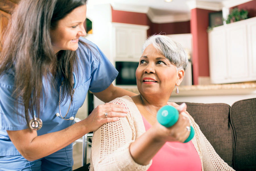Older woman doing physical therapy exercise receives assistance from nurse