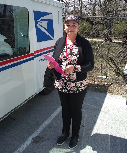 Smiling woman stands next to USPS delivery vehicle
