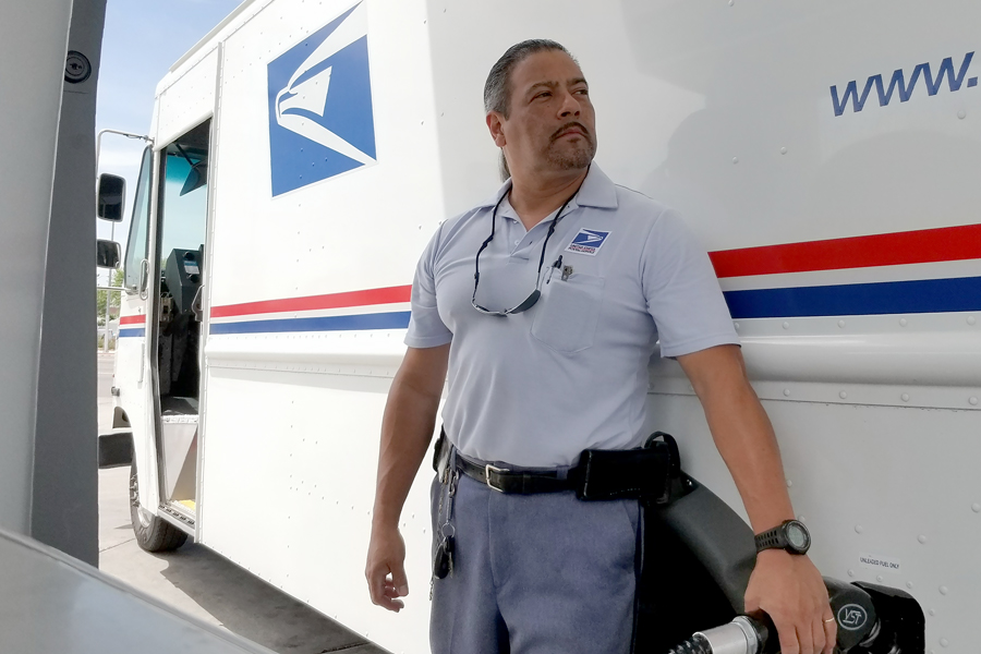 Letter carrier stands near postal vehicle.