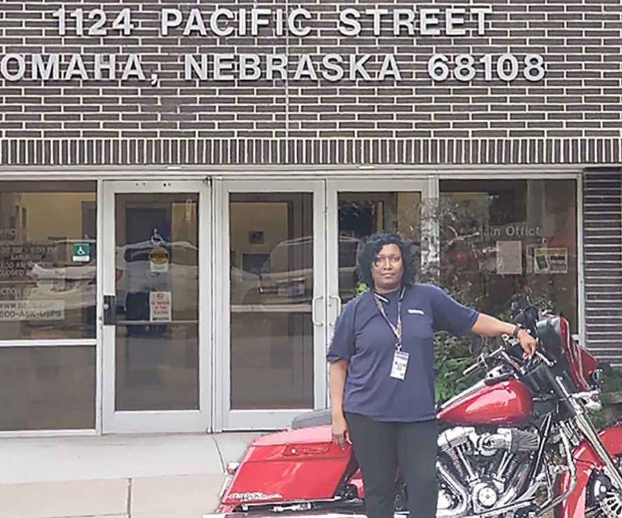 Woman stands near motorcycle in front of Post Office.