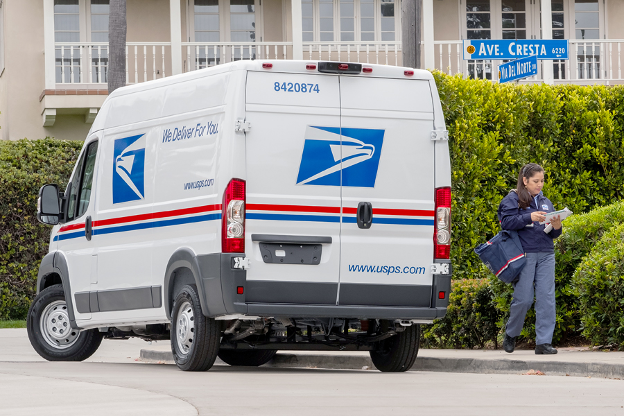 Letter carrier walks near delivery vehicle
