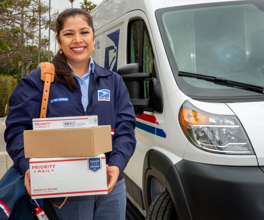 Smiling letter carrier stands next to USPS delivery vehicle