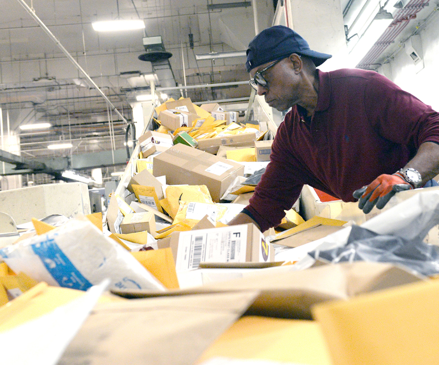 Postal worker sorts mail on conveyor belt inside processing plant