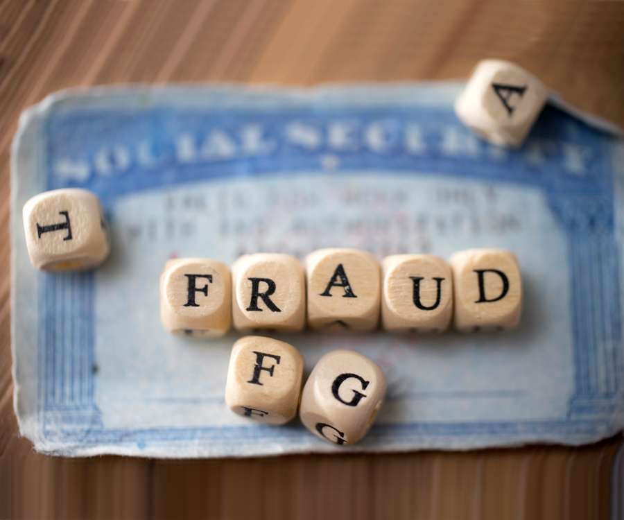 Social Security card under game piece letters spelling the word fraud
