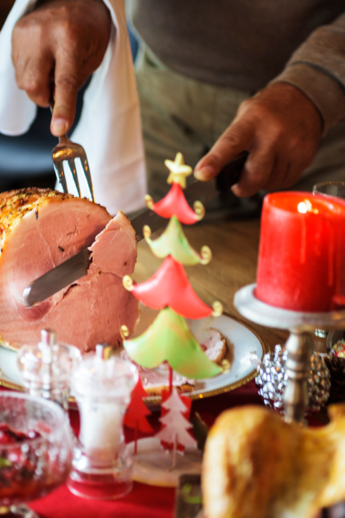 Man's hands slice ham on table with festive decor
