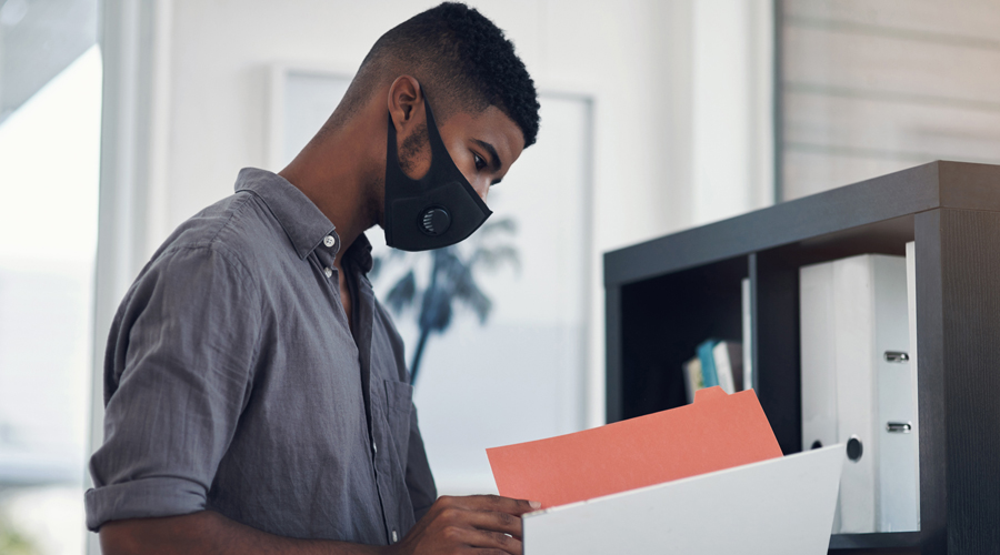 Masked employee examines folder near file cabinet
