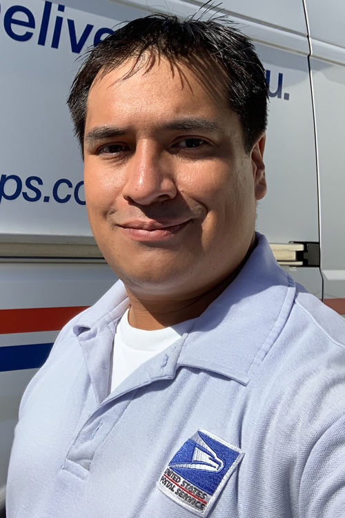 Smiling worker stands next to postal delivery vehicle