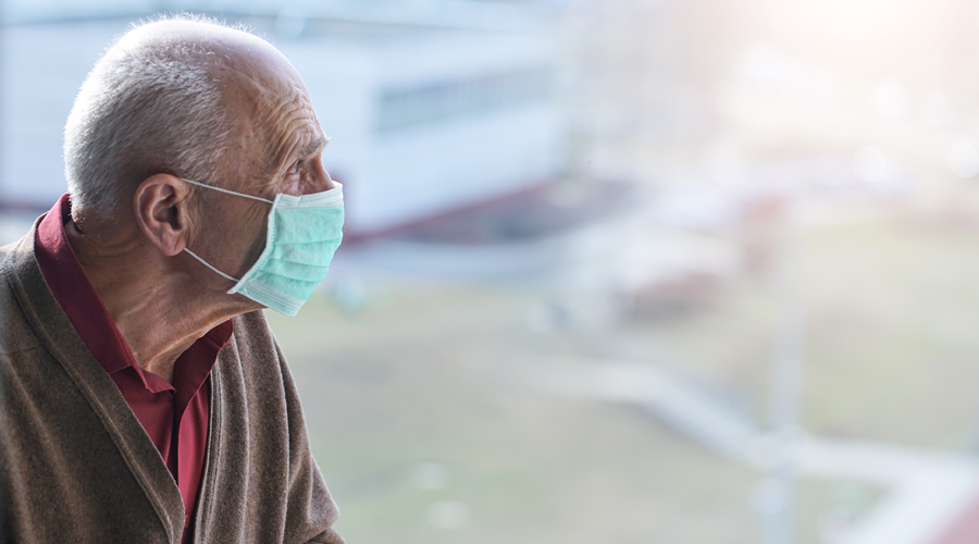 Elderly, masked man looks out window