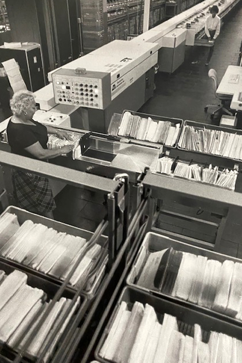 Woman operates mail-sorting machinery on workroom floor