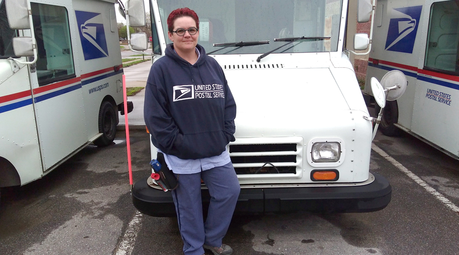 Smiling postal worker stands in front of delivery vehicle