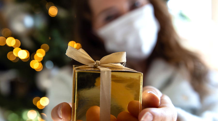 Masked woman presents gift near Christmas tree