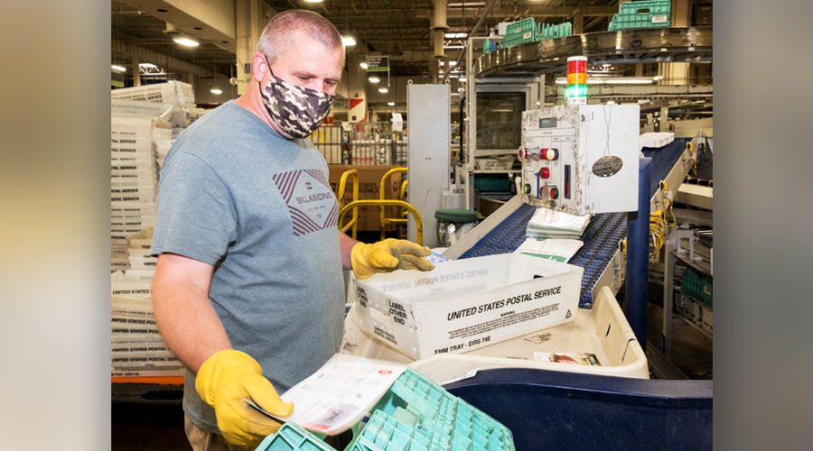 Masked postal worker handles mail on workroom floor